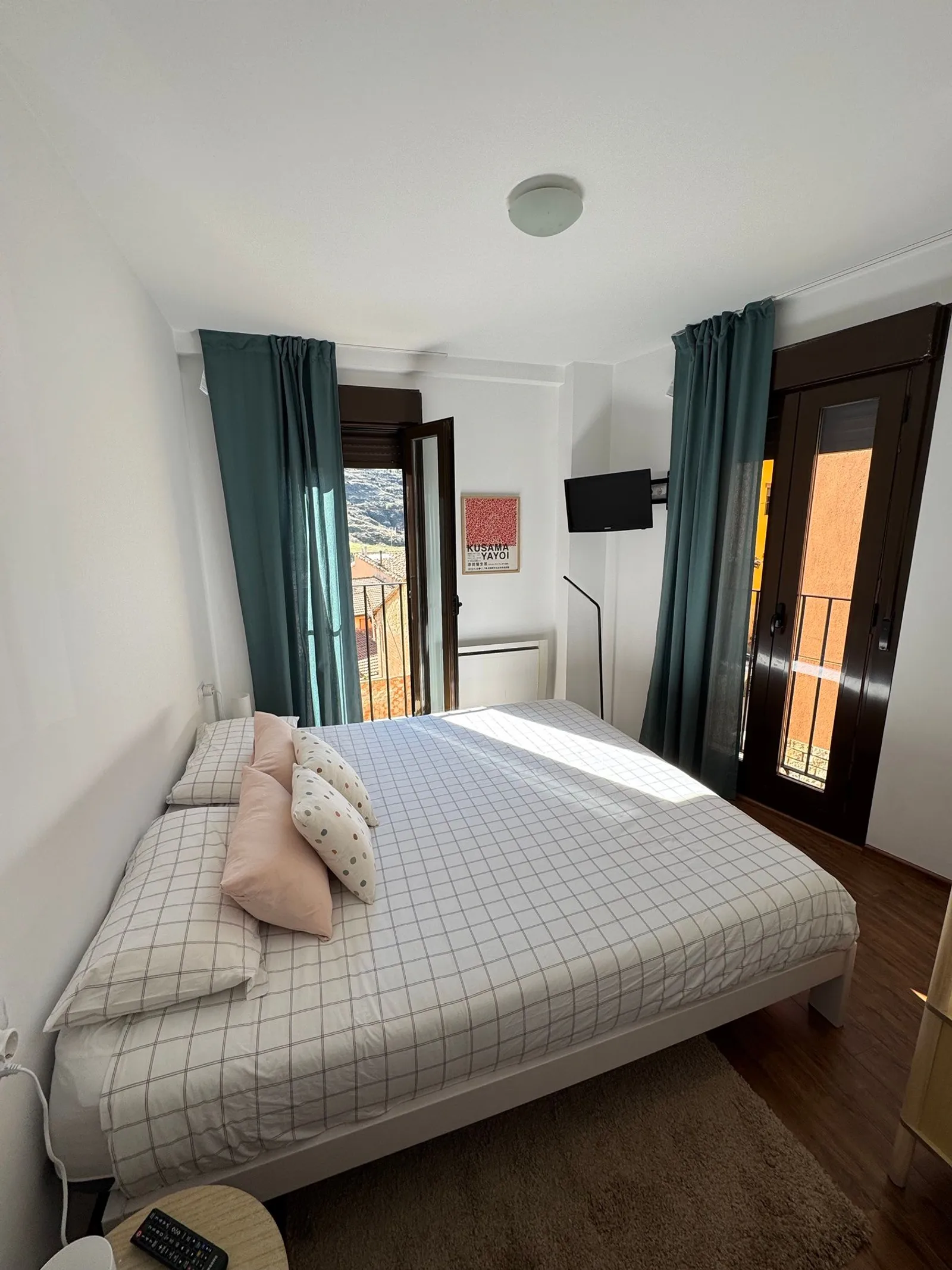 Dormitorio principal con cama doble grande, dos puertas balconeras abiertas al sol y vistas a los tejados de Camarena y a la montaña