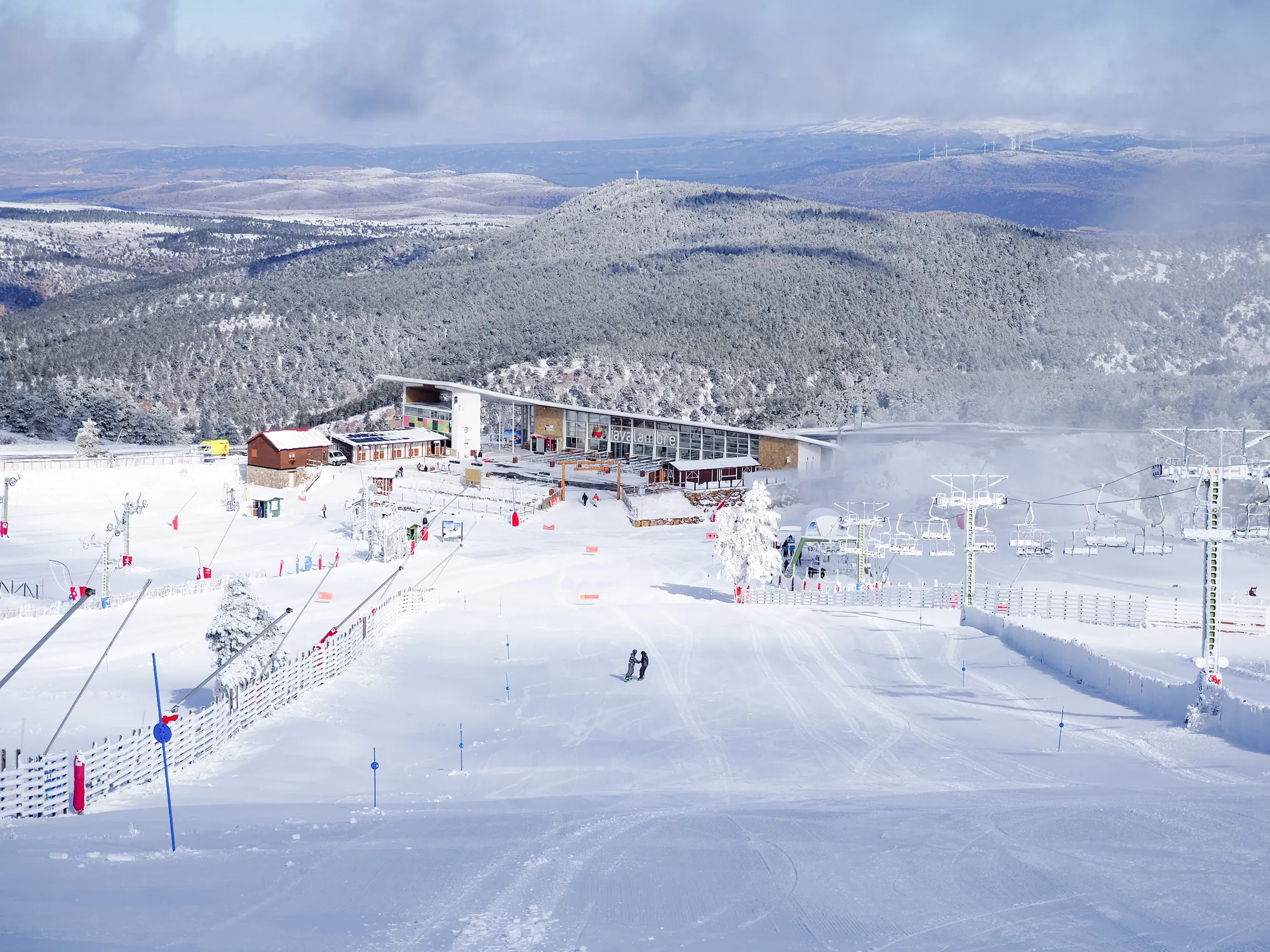 Pistas nevadas, telesillas y edificio de servicios de la estación de esquí de Javalambre, con la montaña al fondo