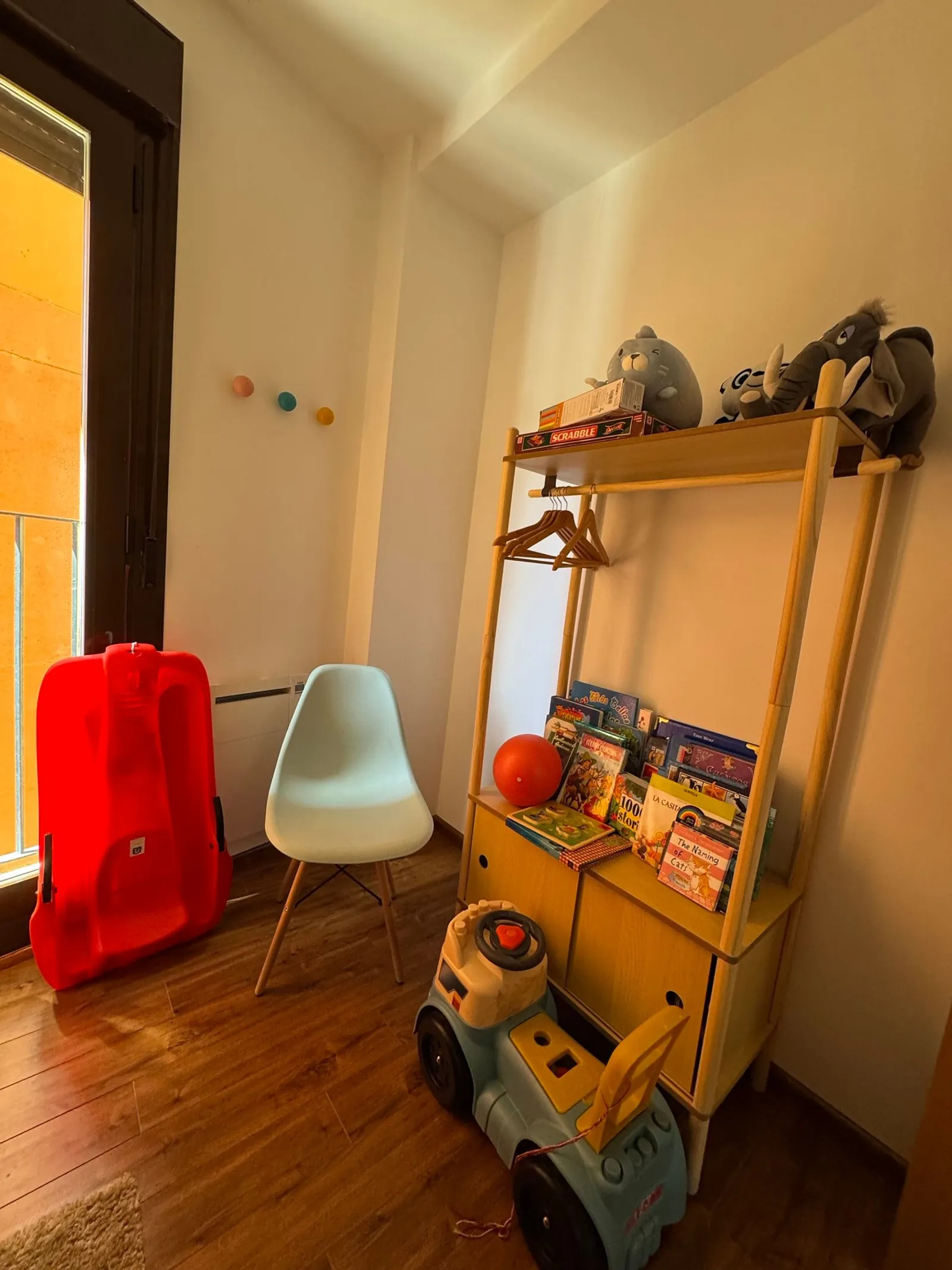 Rincón de juego infantil con estantería de cuentos, juegos de mesa, peluches, correpasillos y un trineo rojo