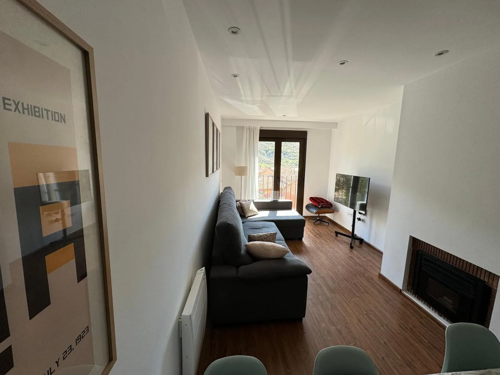 Zona de estar del apartamento con sofá, chimenea de pellets y salida al balcón con vistas al pueblo y a la sierra