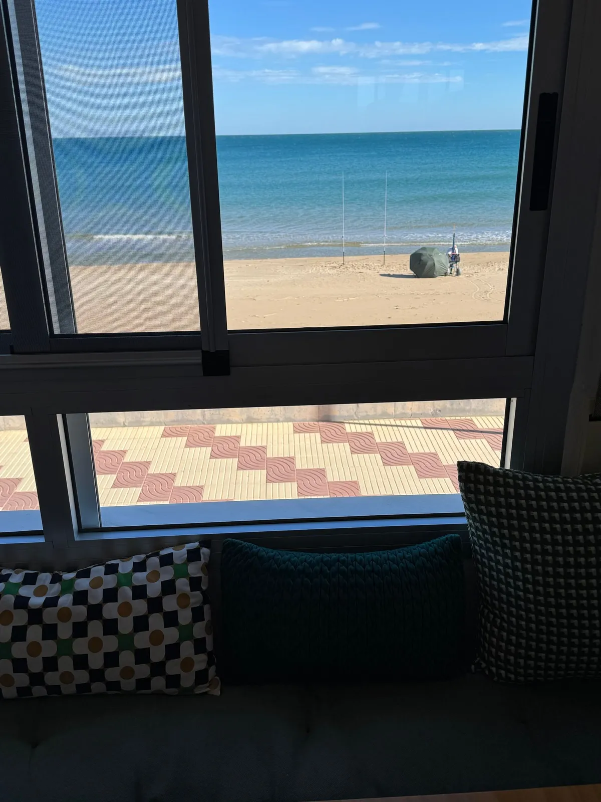 Pescador de surfcasting con sus cañas en la orilla de la playa de la Llastra, visto desde el ventanal del apartamento Valencia Frente al Mar